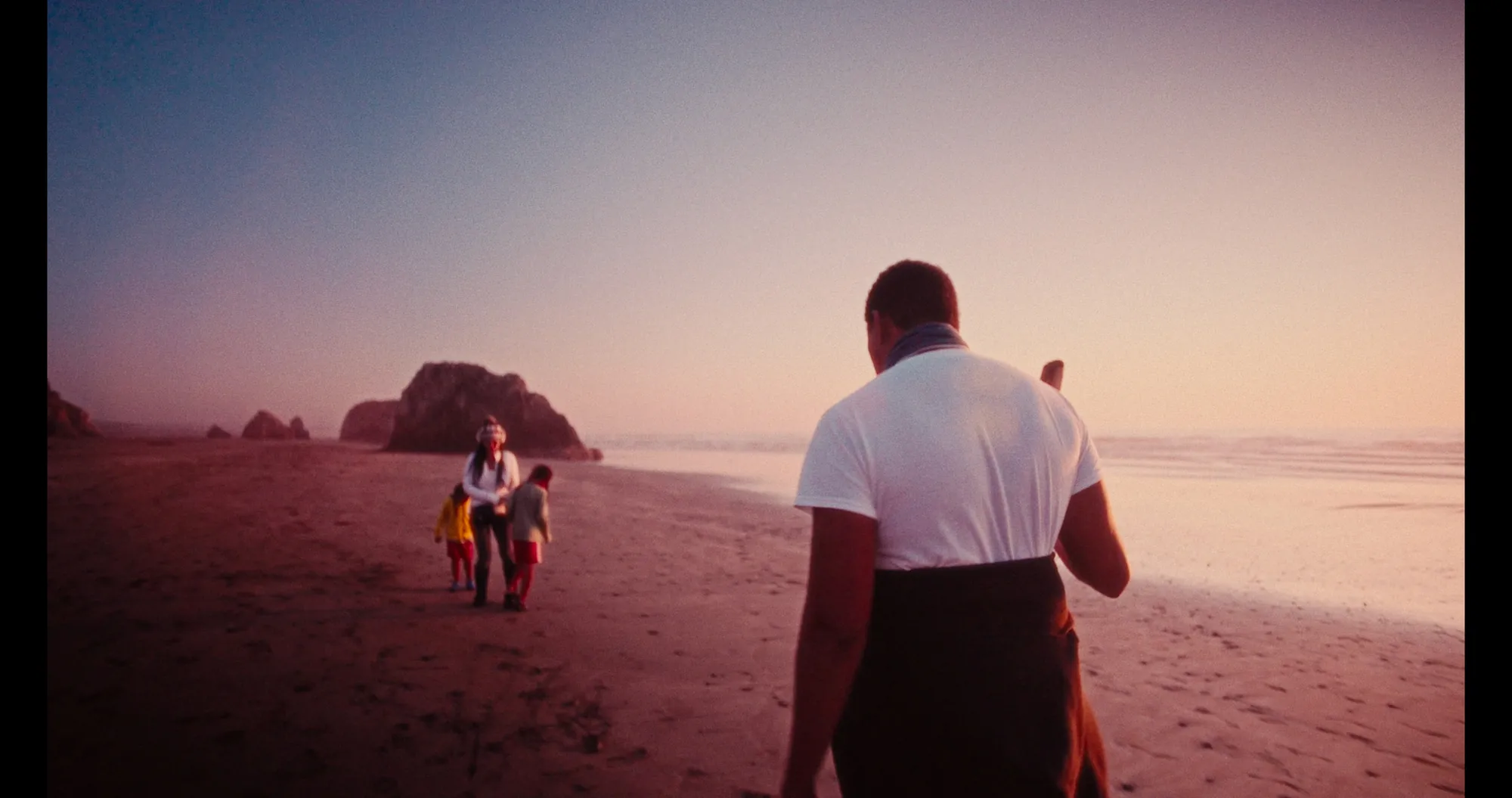 A man walks toward two figures on a beach at dusk, from The Flower Unfolds